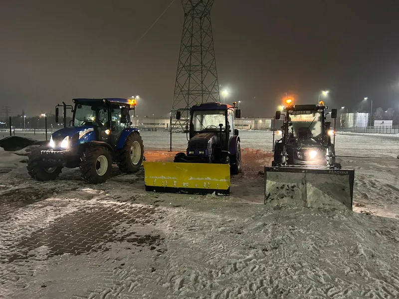 Trzy ciągniki odśnieżające plac nocą